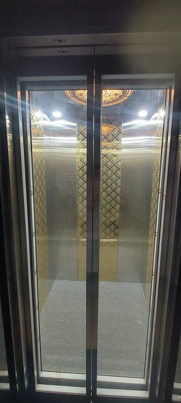 Elevator cabin with glass doors and patterned gold wall panels